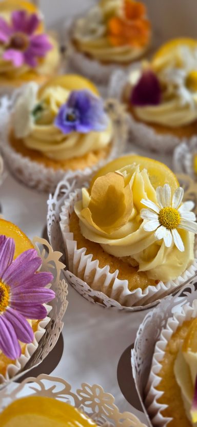 Colourful cupcakes topped with floral decorations in a white baking case.
